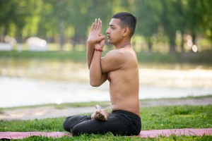 Serene Indian young man practicing yoga fitness or pilates on red mat in park doing variation of Padmasana (virabhadra Padmasana) Lotus Pose with Eagle Arms full length side view